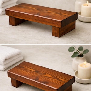 May include: A rectangular wooden riser with a dark brown stained finish and visible wood grain. The stand features a flat top surface supported by two thick, block-style legs on either end, providing a stable elevated platform for display.