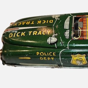 以下が含まれることがあります： 「Dick Tracy Police Dept Squad Car No. 1」と書かれた、緑色のヴィンテージのゼンマイ式ブリキ製おもちゃの車。車体には黄色とオレンジ色のチェック柄の屋根、側面に金属製のゼンマイ用キー、キャラクターのイラストが描かれた黄色い盾型のエンブレムが付いています。