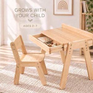 May include: A light-coloured wooden desk and matching chair set. The desk features a pull-out drawer containing small items. Text on the image reads: GROWS WITH YOUR CHILD, AGES 2-7. The furniture has a natural wood finish and metal hardware.