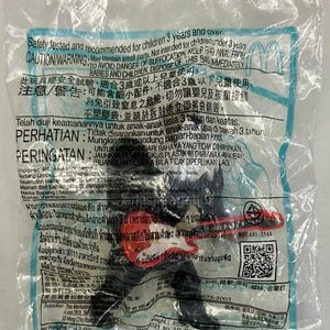 May include: A black plastic figurine of a character playing a red electric guitar, sealed inside a clear plastic bag. The packaging features extensive safety warnings in multiple languages, a QR code, and printed text detailing product information.