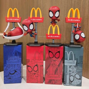 May include: Four McDonald's Spider-Man collectible figures, each featuring a stylized red and blue character on a base with a McDonald's sign. The figures show Spider-Man in various poses, including resting in a hammock, climbing, sitting, and hanging, all packaged in colorful rectangular boxes.