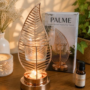 Peut inclure: Un brûle-parfum en métal doré rose avec une structure en forme de feuille et une coupelle en verre transparent pour huiles essentielles. La base accueille une bougie chauffe-plat. L'emballage indique PALME A Scent Burner Inspired by Nature.