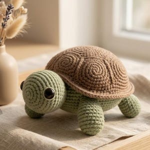 May include: A crocheted turtle toy featuring a light green body and a textured brown shell with spiral patterns. The turtle has large, dark, round eyes and is crafted with visible yarn stitches, showcasing a soft, rounded form and detailed shell design.