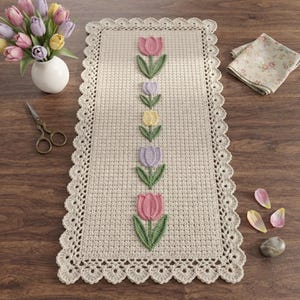 Peut inclure: Un chemin de table rectangulaire en crochet beige orné d'une rangée verticale centrale de cinq tulipes appliquées roses, lavande et jaunes avec des tiges et des feuilles vertes. Le chemin présente une bordure festonnée en crochet.