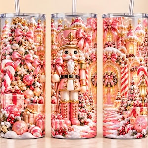 Op de afbeelding: Een cilindervormige beker met rietje in een roze en wit kerstthema. Het ontwerp toont een notenkraker, versierde kerstbomen, ingepakte cadeaus, zuurstokken en een feestelijk gebouw met strikken, alles uitgevoerd in diverse tinten roze.