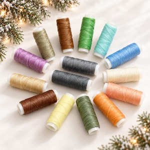 May include: A collection of fifteen cylindrical spools of thread arranged in a circular pattern. The spools feature various solid colors including brown, green, blue, purple, yellow, orange, cream, and gray, each wound with textured thread.