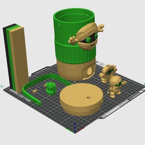 以下が含まれることがあります： 3Dプリントされた緑とベージュの円筒形容器。緑色の目をしたミイラのキャラクター、同色のベージュの蓋、緑色のハンドル、2体の小さなミイラのフィギュアが含まれています。各パーツは黒いグリッド状のプリントベッド上に配置されています。