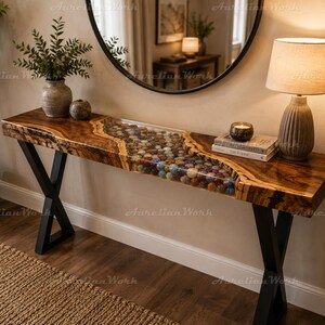 May include: A rectangular console table featuring a live-edge wood slab with a central river inlay filled with multicoloured polished gemstones encased in clear resin. The table is supported by two black metal X-shaped legs.