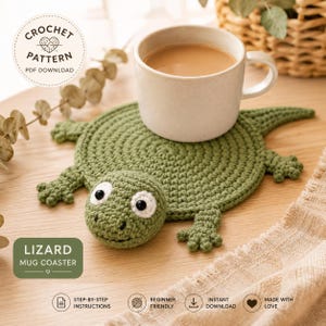 May include: A green crocheted lizard-shaped mug coaster with a round body, four small feet, and a head featuring white eyes with black pupils. A beige ceramic mug sits on the coaster. Text on the image reads CROCHET PATTERN PDF DOWNLOAD and LIZARD MUG COASTER.