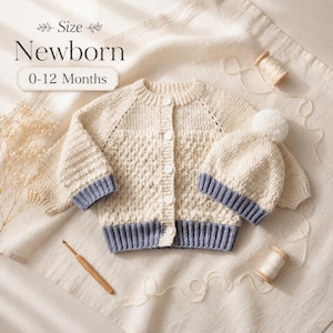 May include: A cream-colored crocheted cardigan with a button-down front and a matching beanie with a white pom-pom. Both items feature blue ribbed cuffs and trim. The text "Size Newborn 0-12 Months" is visible in the upper left corner of the image.