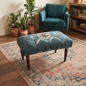 May include: A rectangular ottoman featuring a teal fabric top with a central geometric pattern in cream, navy, and light blue. The piece is supported by four dark brown wooden legs, providing a stable base for this functional furniture item.