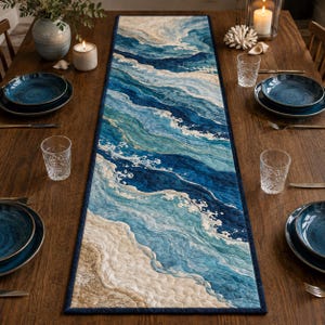 Puede incluir: Un camino de mesa acolchado rectangular con un diseño abstracto de olas oceánicas en tonos azul marino profundo, turquesa y azul claro, que transiciona hacia una orilla de color beige arena, bordeado por un ribete de tela azul oscuro.