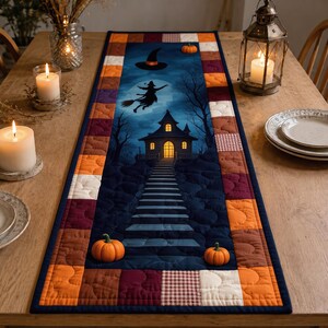 May include: A rectangular quilted table runner featuring a central dark blue panel with a printed scene of a witch flying on a broomstick over a house and a staircase, bordered by a patchwork of orange, burgundy, and white fabric squares.