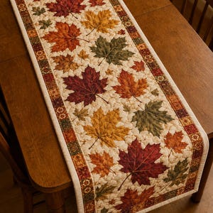 May include: A rectangular quilted table runner featuring a cream-colored background with a repeating pattern of autumn maple leaves in shades of red, orange, yellow, and green, bordered by a decorative mosaic-style trim in matching fall colors.