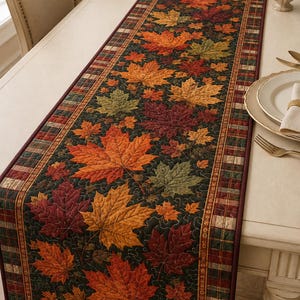 May include: A rectangular quilted table runner featuring a dark green background adorned with a pattern of orange, red, and yellow maple leaves. The runner is bordered by a plaid fabric trim in shades of red, green, and tan, with visible stitching.
