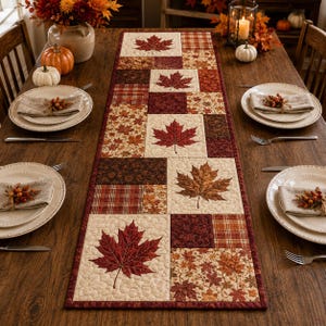 May include: A quilted table runner featuring a patchwork design of autumn leaves, plaid patterns, and solid blocks in shades of cream, burgundy, and brown. The runner is centered on a wooden table with place settings, pumpkins, and floral decor.