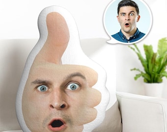 May include: A custom-shaped throw pillow in the form of a thumbs-up hand gesture. The surface of the pillow features a printed photograph of a man's face with a surprised expression, integrated into the skin-toned hand design.