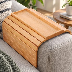May include: A flexible bamboo sofa arm tray featuring a flat rectangular surface with raised edges and a series of connected wooden slats that drape over the side of a couch to provide a stable platform for holding items securely in place.