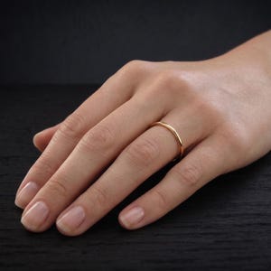 Puede incluir: Un anillo de banda de oro pulido sencillo con una superficie lisa y redondeada. El anillo presenta un perfil fino y minimalista con un acabado en oro amarillo metálico cálido que refleja la luz uniformemente por toda su circunferencia.
