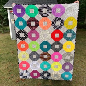 May include: A colorful quilt with a geometric pattern of octagons and squares. The quilt is made with a variety of fabrics, including polka dots, stripes, and floral prints. The quilt is a light gray color with a white border.