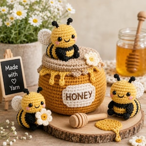 Può includere: Un vasetto di miele all'uncinetto con coperchio, un'ape gialla e nera sopra, due api aggiuntive, un mestolo per miele in legno e un piccolo cartello con la scritta Made with Yarn. Il vasetto ha un'etichetta bianca con la parola HONEY ricamata in marrone.