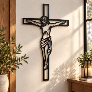 May include: A black metal wall crucifix featuring a stylized cutout silhouette of Jesus Christ on the cross. The design depicts the figure with a crown of thorns and a loincloth, integrated into a simple rectangular cross frame with open spaces.