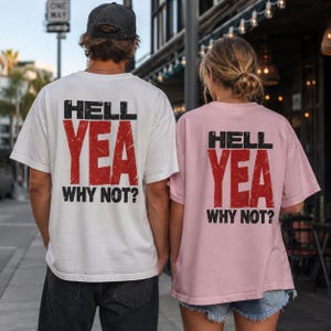 Może przedstawiać: Biały t-shirt i jasnoróżowy t-shirt, oba z nadrukiem HELL YEA WHY NOT? na plecach, wykonanym czcionką w kolorze czarnym i czerwonym z efektem postarzenia. Biała koszulka zestawiona jest z ciemnymi jeansami i czarną czapką, a różowa z jeansowymi szortami.