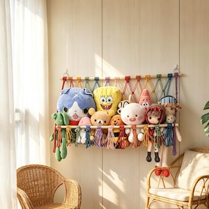 May include: A multi-colored macrame toy hammock suspended by wooden dowels, featuring a woven net design with decorative tassels. The hammock is filled with various plush toys, including a yellow sponge character and a blue cat-like figure.