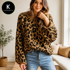 May include: A long-sleeved knit sweater featuring a brown and black leopard print pattern with a crew neckline and ribbed cuffs. The sweater is paired with blue denim jeans. A circular logo in the top left corner displays the text K KINTCRAFTS.