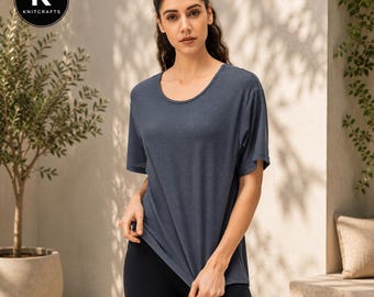 May include: A dark slate blue short-sleeved t-shirt with a subtle textured pattern, featuring a wide round neckline and a relaxed fit. The fabric has a fine, uniform weave visible across the surface, providing a clean and simple appearance.