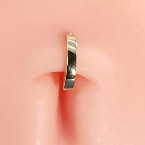 May include: A polished gold-tone curved segment ring designed for body piercing. The jewelry features a smooth, reflective metallic surface and a simple, continuous arc shape that sits securely within the skin fold of the navel area.