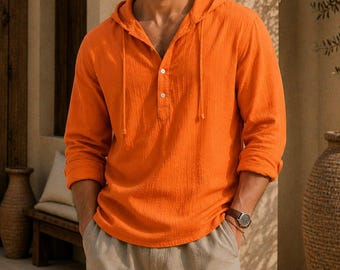 May include: A bright orange long-sleeve hooded shirt featuring a partial button-down placket with two white buttons and matching drawstring cords, paired with light beige trousers. The shirt has a textured fabric finish and cuffed sleeves.