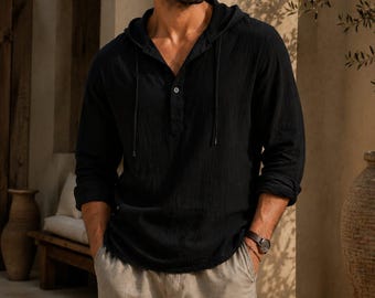 May include: A black long-sleeved hooded shirt with a button-up placket and thin drawstrings, paired with light beige trousers. The shirt features a textured fabric and a relaxed fit, while the trousers have a straight-leg cut and a neutral tone.