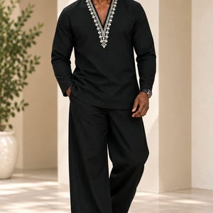 Peut inclure: Une tunique noire à manches longues avec une encolure en V profonde ornée de broderies géométriques blanches, associée à un pantalon noir assorti à jambes larges. L'ensemble est complété par des sandales en cuir marron.