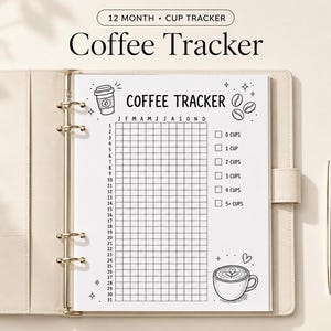 Op de afbeelding: Een wit vel papier met de titel Coffee Tracker in een beige map. De pagina bevat een raster voor 12 maanden en 31 dagen, met selectievakjes voor 0 tot 5+ kopjes. Illustraties tonen een koffiekopje, bonen en een hartje. Een gouden pen ligt ernaast.
