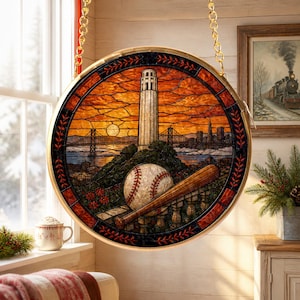May include: A circular stained glass suncatcher featuring a San Francisco cityscape with Coit Tower, the Bay Bridge, a baseball, and a wooden bat. The scene is set against an orange sunset sky, framed by a dark border with red leaf patterns.