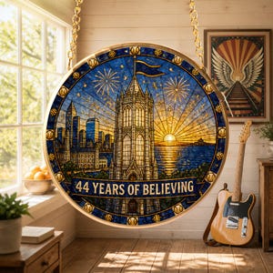 May include: A circular stained glass-style hanging decoration featuring a central tower, a city skyline, a sunset over water, and fireworks. The text 44 YEARS OF BELIEVING is printed in a banner at the bottom. It is suspended by gold chains.