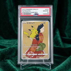 Könnte beinhalten: Eine 2021 Pokemon JPN.S-P #227 Pikachu Pokemon Stamp Box Sammelkarte mit der Bewertung GEM MT 10. Die Karte zeigt einen gelben Pikachu-Charakter, der auf dem Rücken einer Person in einem roten Kimono mit Muster und grünem Obi vor Gold sitzt.