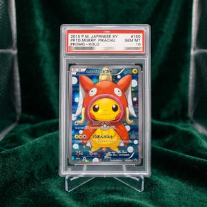 May include: A 2015 Japanese XY Pikachu promo trading card, graded GEM MT 10 by PSA. The card features Pikachu wearing a red Magikarp costume, encased in a clear plastic protective slab with a label at the top displaying the card details and grade.
