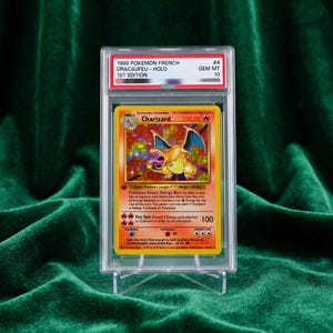 Może przedstawiać: Karta kolekcjonerska Pokemon Charizard z 1999 roku, 1. edycja, zamknięta w przezroczystym etui ochronnym. Karta zawiera holograficzną ilustrację pomarańczowego smoka oraz tekst, w tym 120 HP, Fire Spin i Energy Burn, z oceną stanu GEM MT 10.