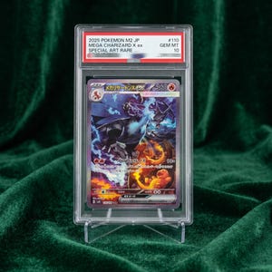 May include: A graded 2025 Pokemon M2 JP Mega Charizard X ex Special Art Rare trading card in a clear plastic slab. The label reads 2025 POKEMON M2 JP MEGA CHARIZARD X EX SPECIAL ART RARE #110 GEM MT 10. The card features a dark dragon with blue flames.