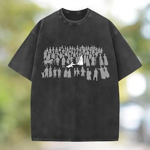 Könnte beinhalten: Ein anthrazitfarbenes Kurzarm-T-Shirt mit einem weißen Grafikdruck, der eine große Menschenmenge aus stilisierten Figuren zeigt. Das Design umfasst zahlreiche Personen in Reihen, einige mit Stäben, sowie die Silhouette eines Tieres.