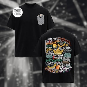 May include: A black short-sleeve t-shirt featuring a small graphic on the front pocket area of a figure behind a brick wall. The back displays colorful, intricate typography and illustrations including a crown, a flag, and a hamster.
