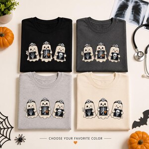 Op de afbeelding: Vier T-shirts met ronde hals in zwart, donkergrijs, lichtgrijs en crème, elk met een afbeelding van drie cartoongeesten die hoofdspiegels dragen en röntgenfoto's van een hand, een borstkas met pompoen en een schedel vasthouden.