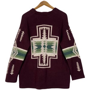 Peut inclure: Un pull en tricot à manches longues de couleur bordeaux profond, orné d'un grand motif géométrique en forme de croix centré au dos. Le design intègre des nuances de crème, de vert clair et de vert foncé dans un motif angulaire répété.
