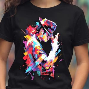 May include: A black short-sleeved t-shirt featuring a vibrant, multi-colored graphic print of a figure wearing a fedora and a single glove, rendered in a stylized, abstract paint-splatter design with bright hues of blue, pink, yellow, and red.