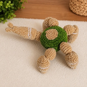 May include: A plush toy shaped like a turtle with a round, textured green shell and tan limbs, head, and tail. The limbs and head are crafted from soft, velvety yarn, featuring white stitched details on the appendages and a circular tan patch.