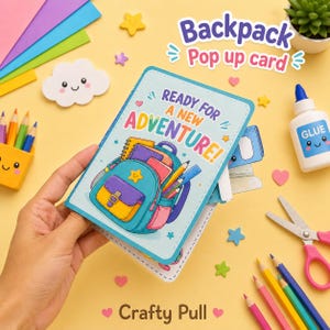 May include: A light blue pop-up card featuring a colorful illustration of a backpack filled with school supplies and the text READY FOR A NEW ADVENTURE. The card is rectangular with rounded corners and a stitched border design on a yellow surface.