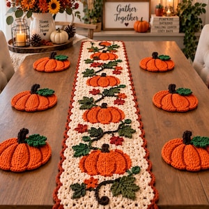 Puede incluir: Un camino de mesa largo de ganchillo en color crema con un patrón repetitivo de calabazas naranjas con hojas verdes y enredaderas marrones, acompañado de seis posavasos de ganchillo a juego con forma de calabaza.