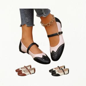 May include: A pair of two-tone Mary Jane flats featuring a black cap toe with decorative perforations, a light pink or white body, and a thin black buckled strap across the instep. Additional color variations include brown and white or black and white.